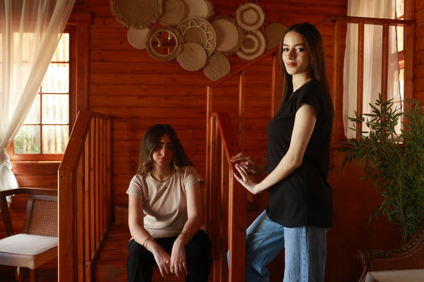Two women in casual t-shirts, one in black and one in beige, in a cozy wooden interior