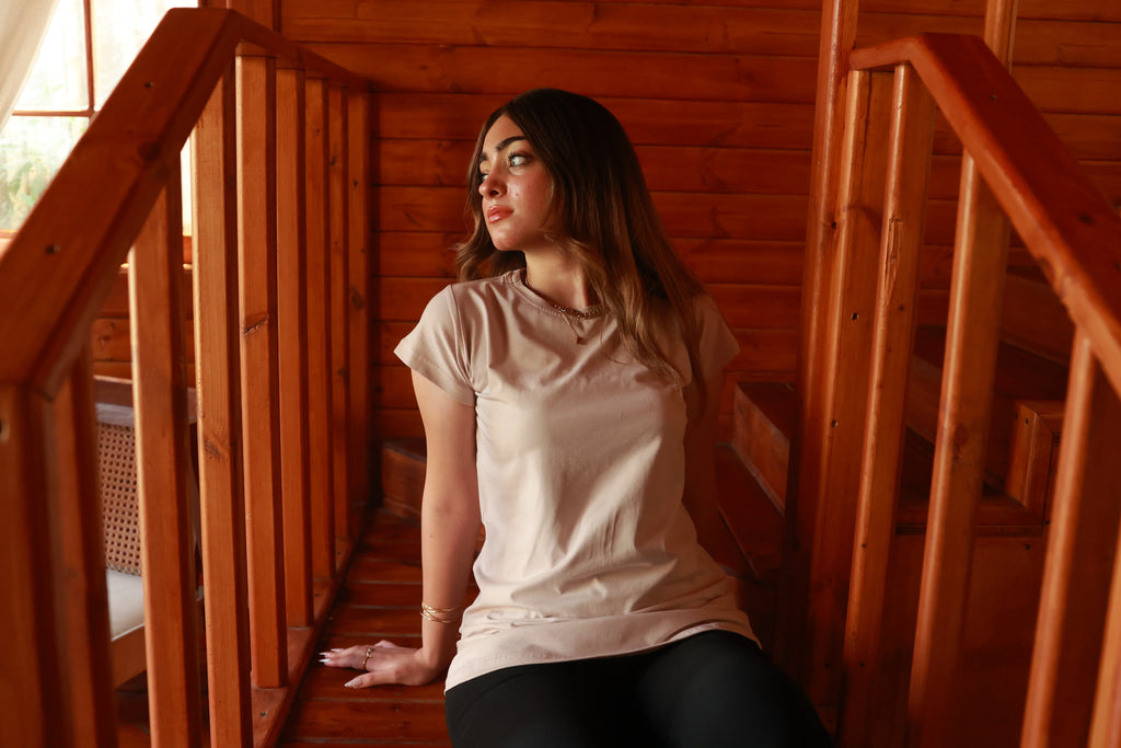 Woman in beige basic t-shirt and black leggings sitting on wooden stairs indoors
