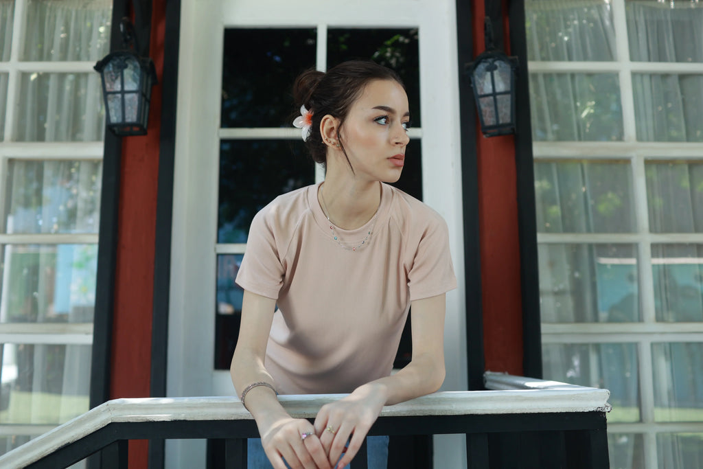 Woman in pale pink basic t-shirt leaning on porch railing, casual summer outfit style