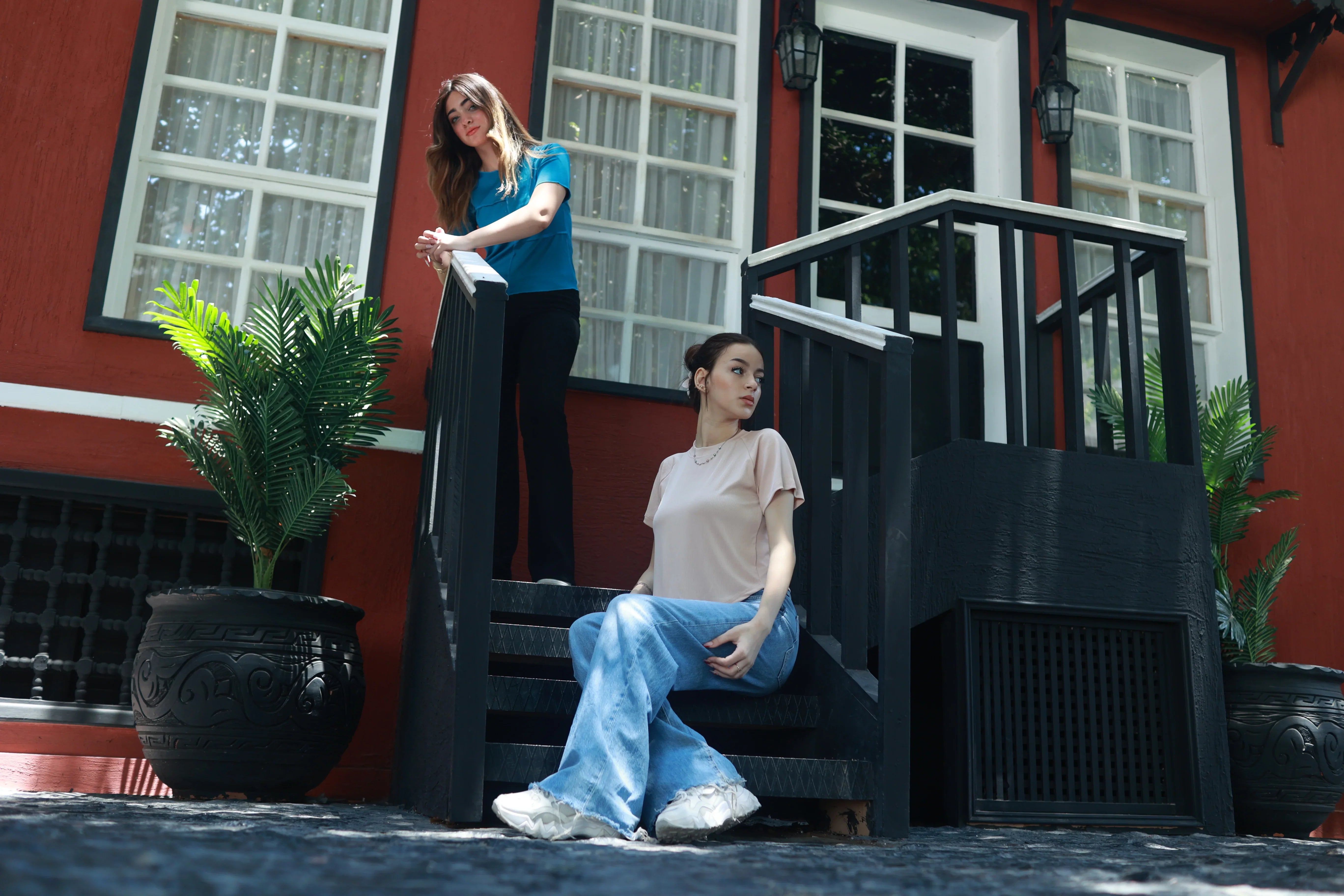 Two women in casual basic t-shirts and jeans on outdoor staircase with potted plants