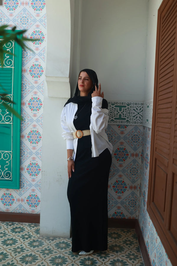 Woman in a black dress with white shirt and belt, standing by colorful patterned tiles