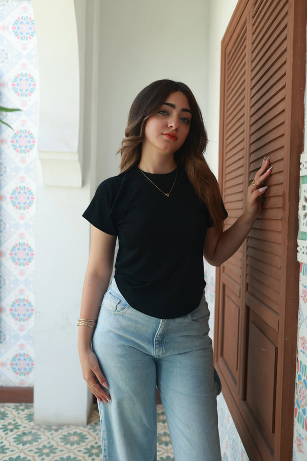 Woman in a black basic t-shirt and light blue jeans standing indoors with patterned tiles
