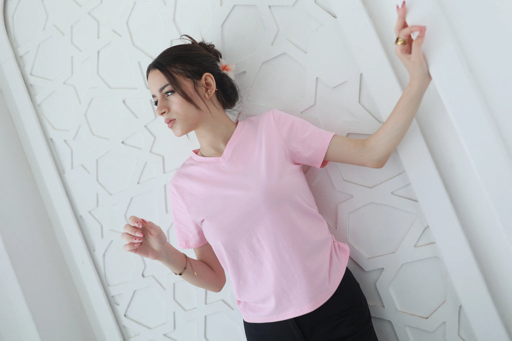 Woman in a pink basic t-shirt with short sleeves, standing by a white geometric wall