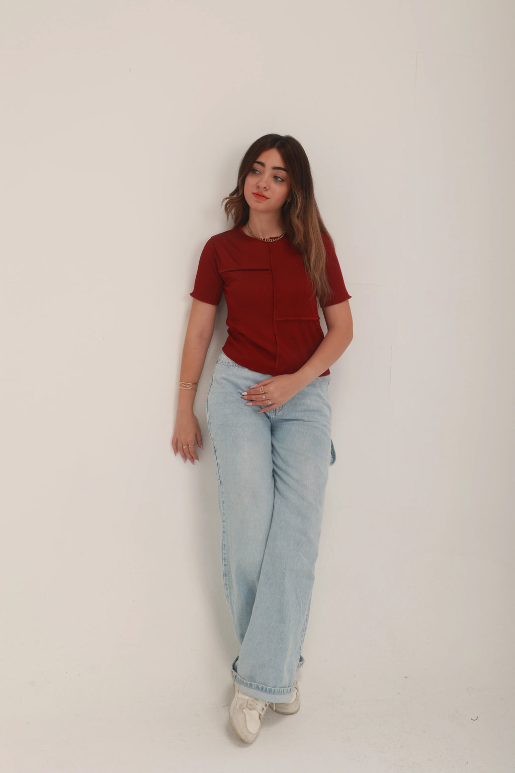 Woman in casual red top and light blue jeans standing against a plain white background
