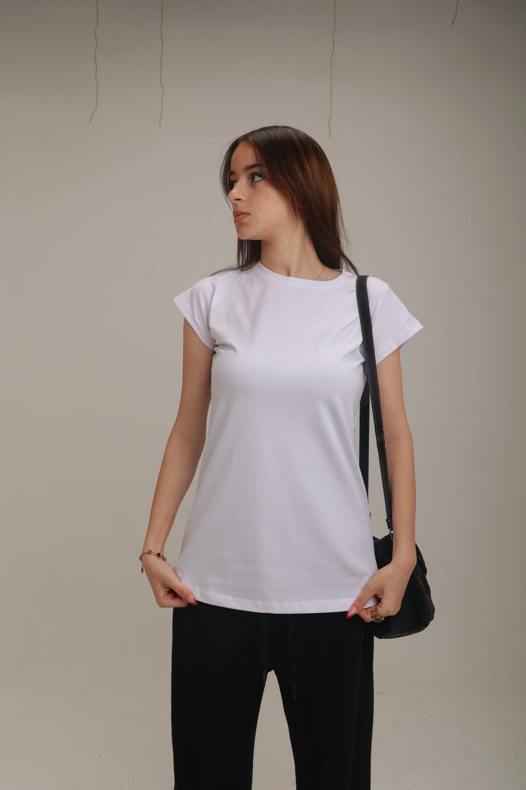 Woman wearing a basic white t-shirt and black pants with a shoulder bag in studio