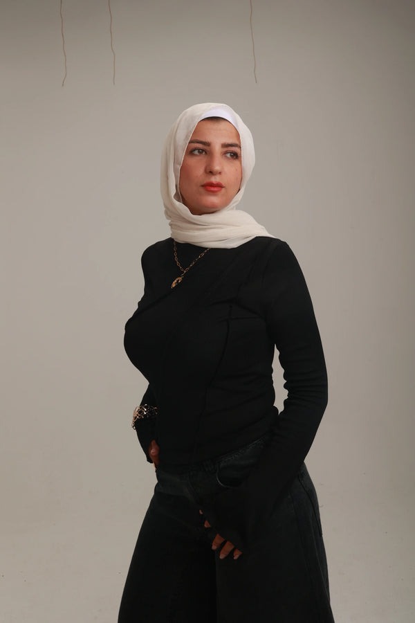 Woman in white headscarf, black long sleeve top, and dark jeans posing in studio