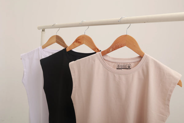 Sleeveless cotton tops in white, black, and beige on wooden hangers on a rack