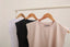 Sleeveless cotton tops in white, black, and beige on wooden hangers on a rack