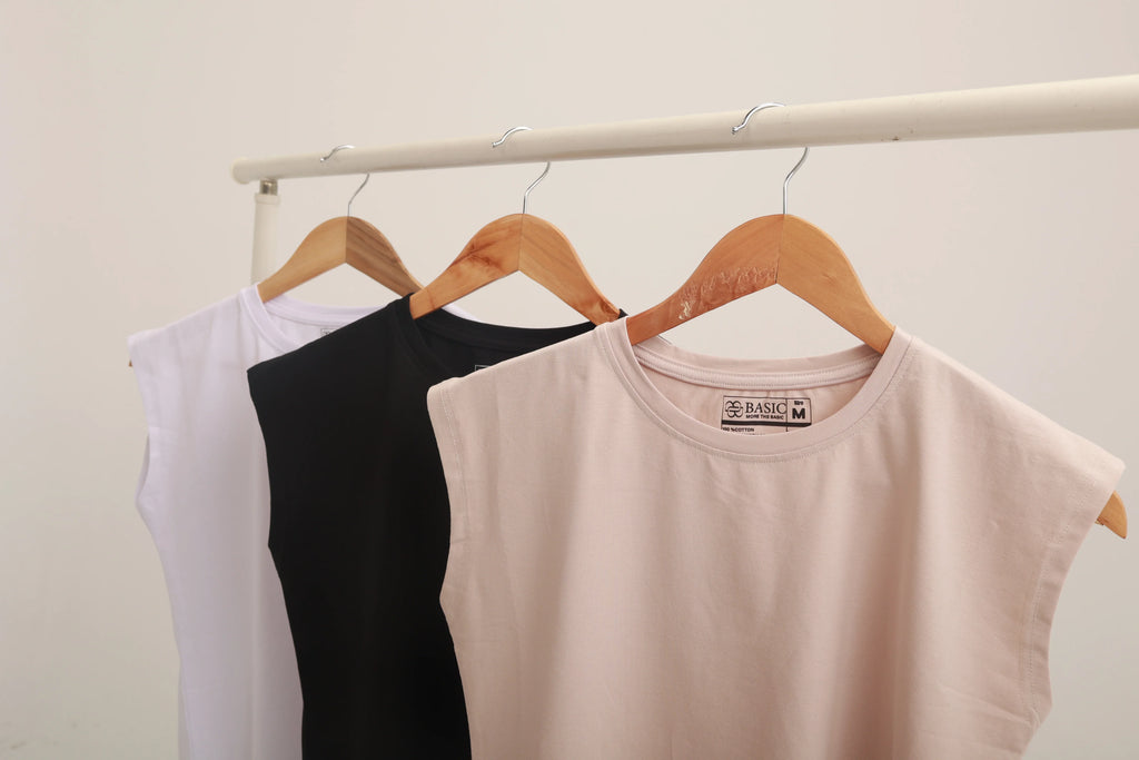 Neutral, black, and white sleeveless cotton tops on wooden hangers against a plain background