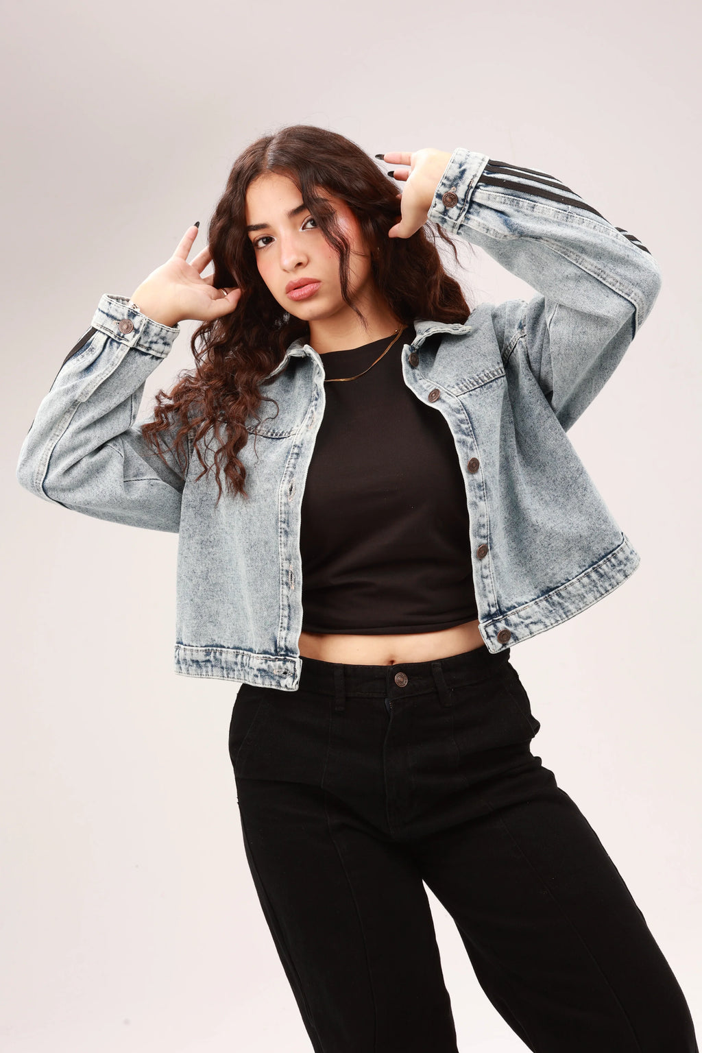 Woman wearing a light denim jacket, black crop top, and black pants in studio