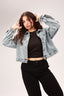 Woman wearing a light denim jacket, black crop top, and black pants in studio