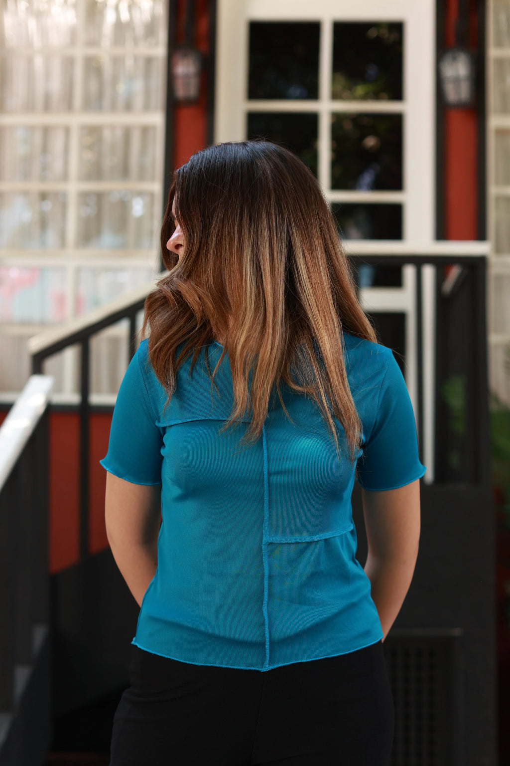 Woman in teal short sleeve top with visible back seam, standing outdoors