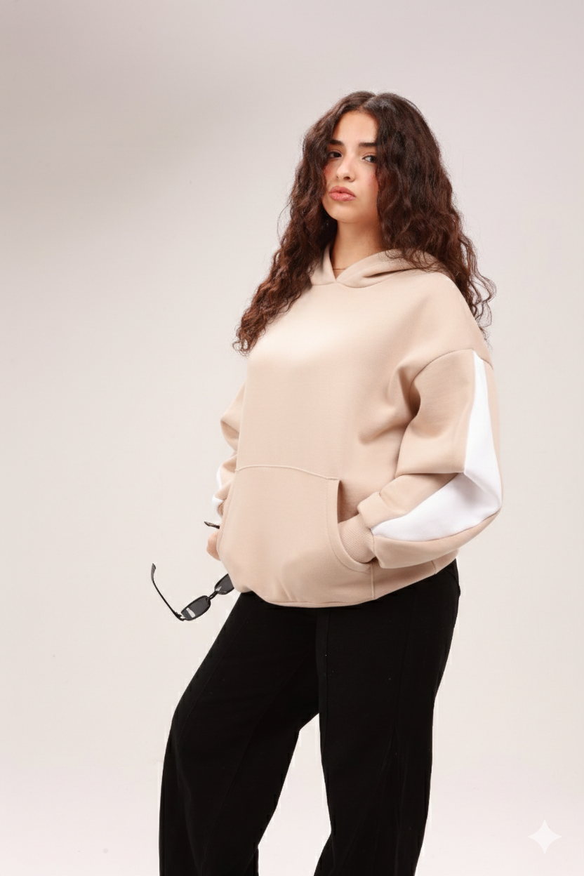 Woman in a beige hoodie with white sleeve accents and black pants holding sunglasses